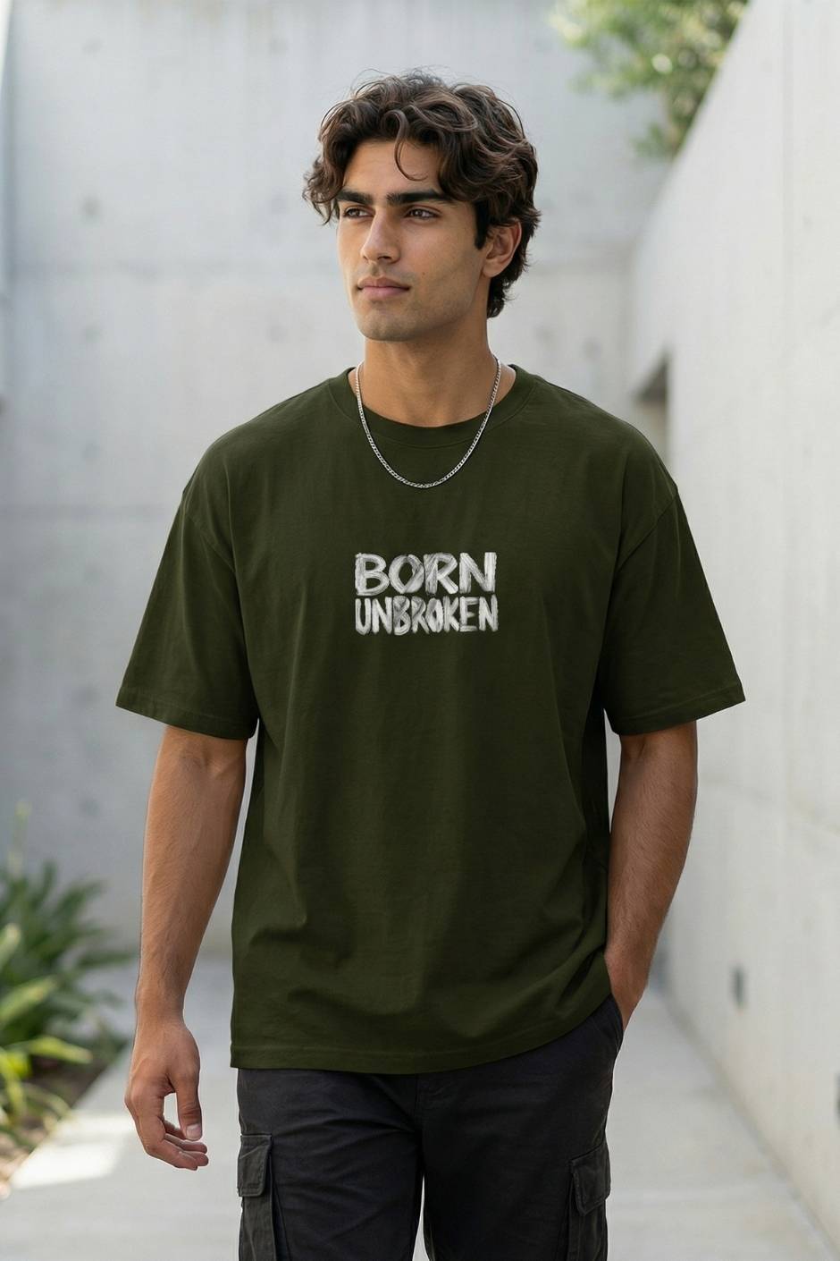 Man wearing a Olive t-shirt with 'BORN UNBROKEN' text, standing outdoors.
