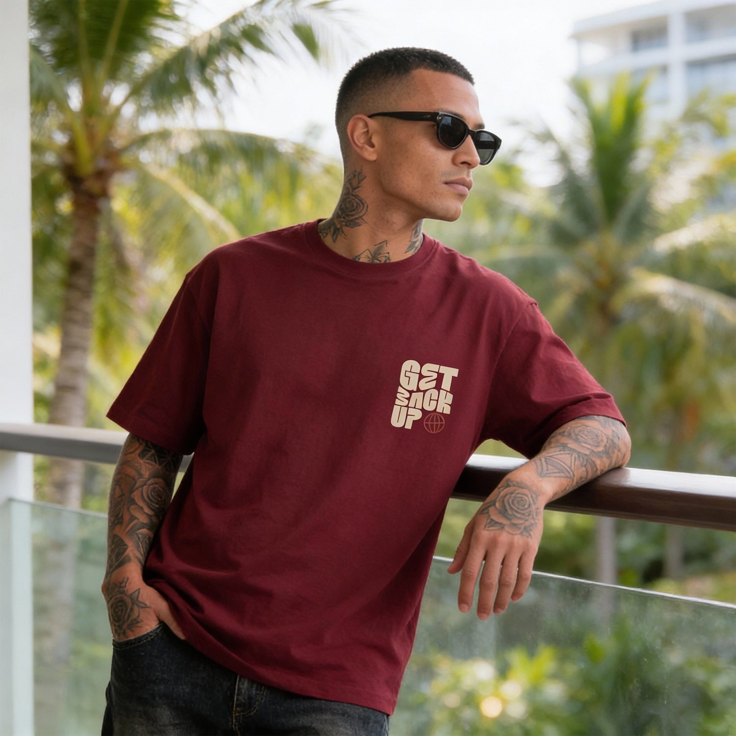 Man wearing a maroon t-shirt with text, standing outdoors with greenery in the background