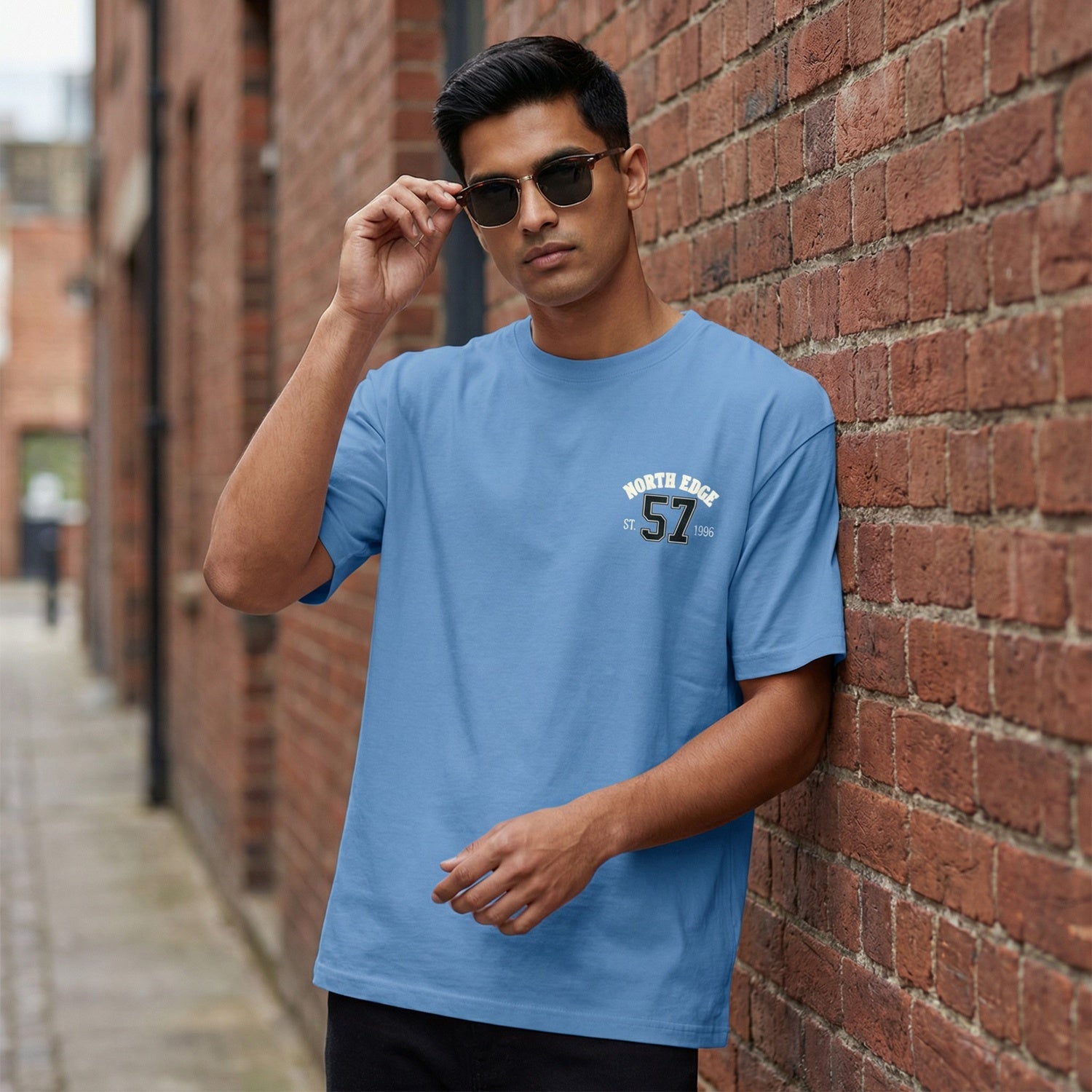 Man wearing a blue t-shirt with text leaning against a brick wall.