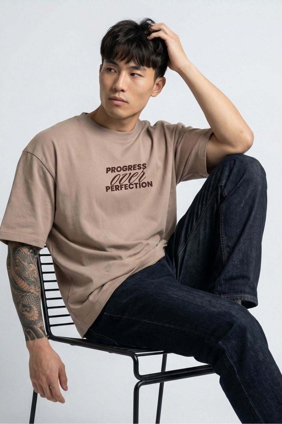 Man sitting on a chair wearing a light beige t-shirt with text, against a plain background