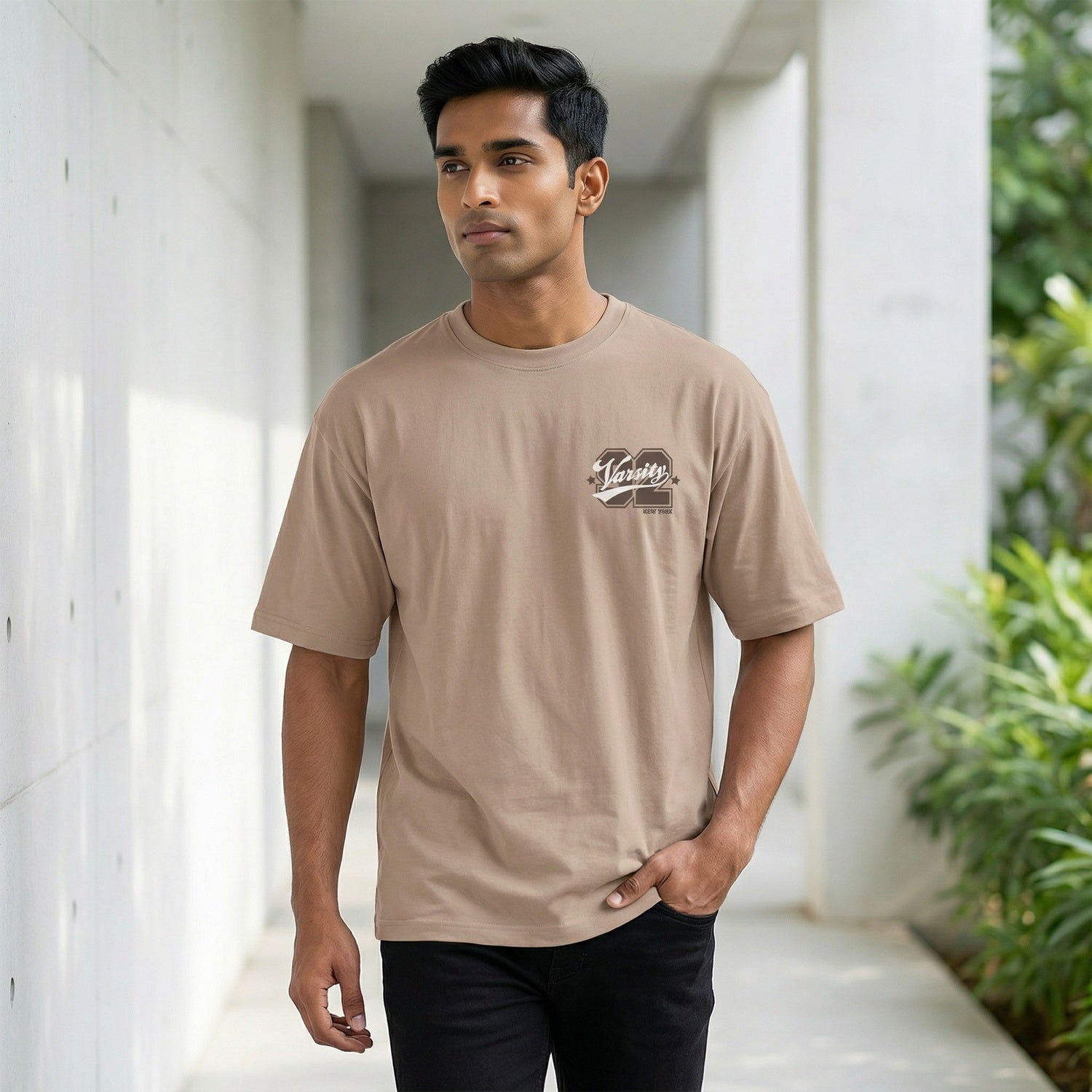 Man wearing a beige t-shirt with a logo, standing in an outdoor setting.