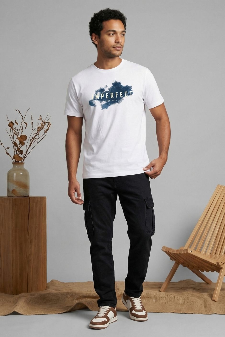 Man wearing a white t-shirt with a blue graphic and text, standing in a room with wooden furniture and decor.