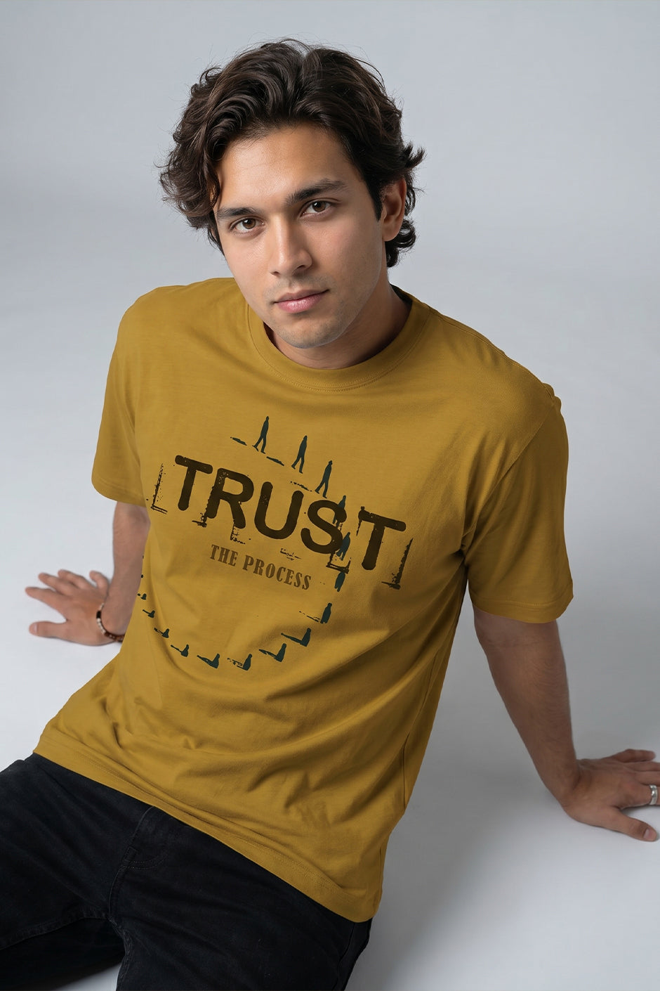 Man wearing a mustard yellow t-shirt with 'TRUST THE PROCESS' text on a white background