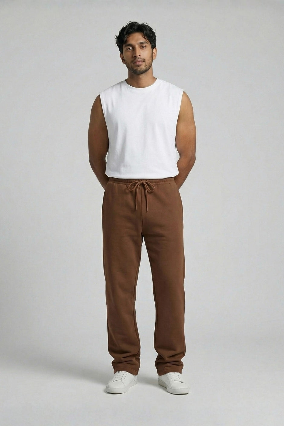 Man wearing a white sleeveless shirt and brown jogger on a plain background
