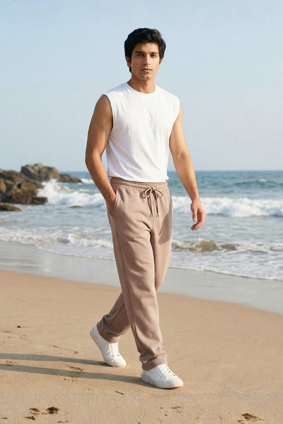 Man walking on a beach wearing a white sleeveless shirt and light beige jogger.