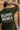 Person wearing a olive t-shirt with 'Born Unbroken' text on the back, standing against a wooden wall.
