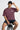 Person wearing a plum t-shirt with text and black shorts, sitting on a stool against a white background