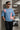 Man wearing a light blue t-shirt with graphic designs, standing against a concrete wall.