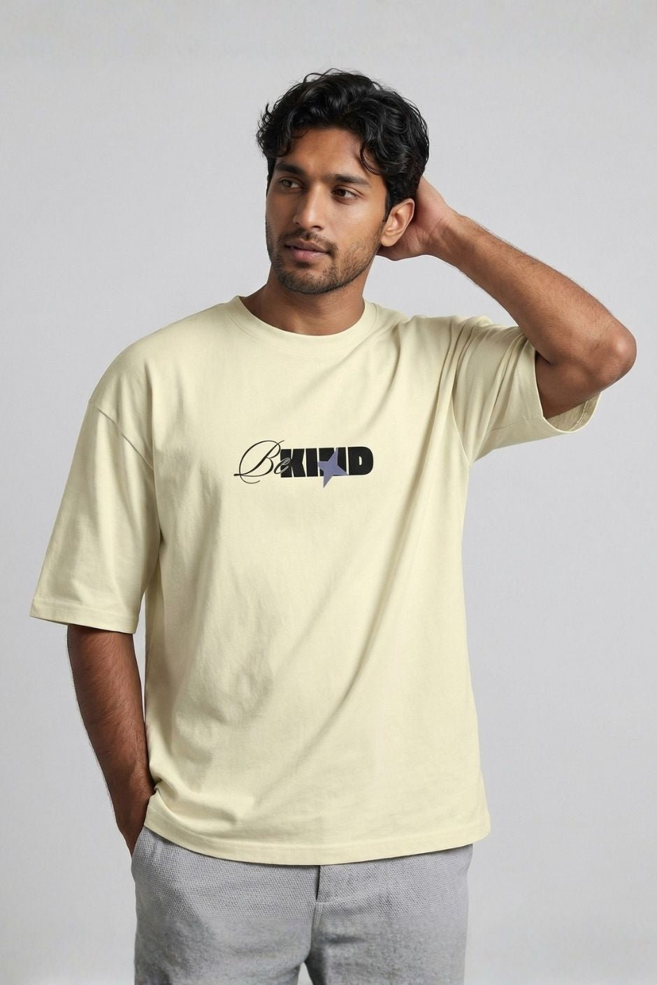 Man wearing a off white t-shirt with 'Be Kind' text on a plain background