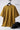 Mustard yellow t-shirt with 'community' text on a hanger, next to a black cap on a white background.