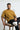 Man wearing a mustard yellow oversized t-shirt sitting on a chair with text annotations on a white background