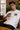 Person wearing a white t-shirt with a logo, holding a coffee cup indoors.