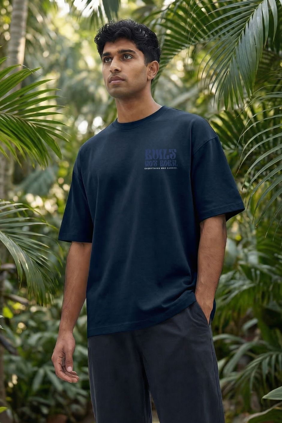 Man wearing a pastel blue t-shirt with text standing among tropical plants