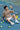 Person sitting on a tennis court with tennis balls around, holding a ball.