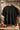 Black t-shirt with 'raax' logo on a wooden hanger against a wooden wall.