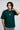 Man wearing a bottle green t-shirt with a logo, standing against a plain background