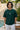 Man wearing a bottle green t-shirt with a logo, standing by a pool with a stone wall and plants in the background.