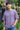 Man wearing a lilac t-shirt standing outdoors with greenery and flowers in the background