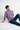 Man wearing a lilac t-shirt and blue jeans sitting on a white background