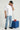 Person wearing a white t-shirt and blue jeans, holding a red telephone, standing next to a blue cube on a plain background.