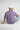 Person wearing a lilac 'RAAX' t-shirt sitting on the ground with a white background