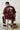 Person wearing a rust t-shirt with motorcycle graphic and text, sitting on a wooden stool.