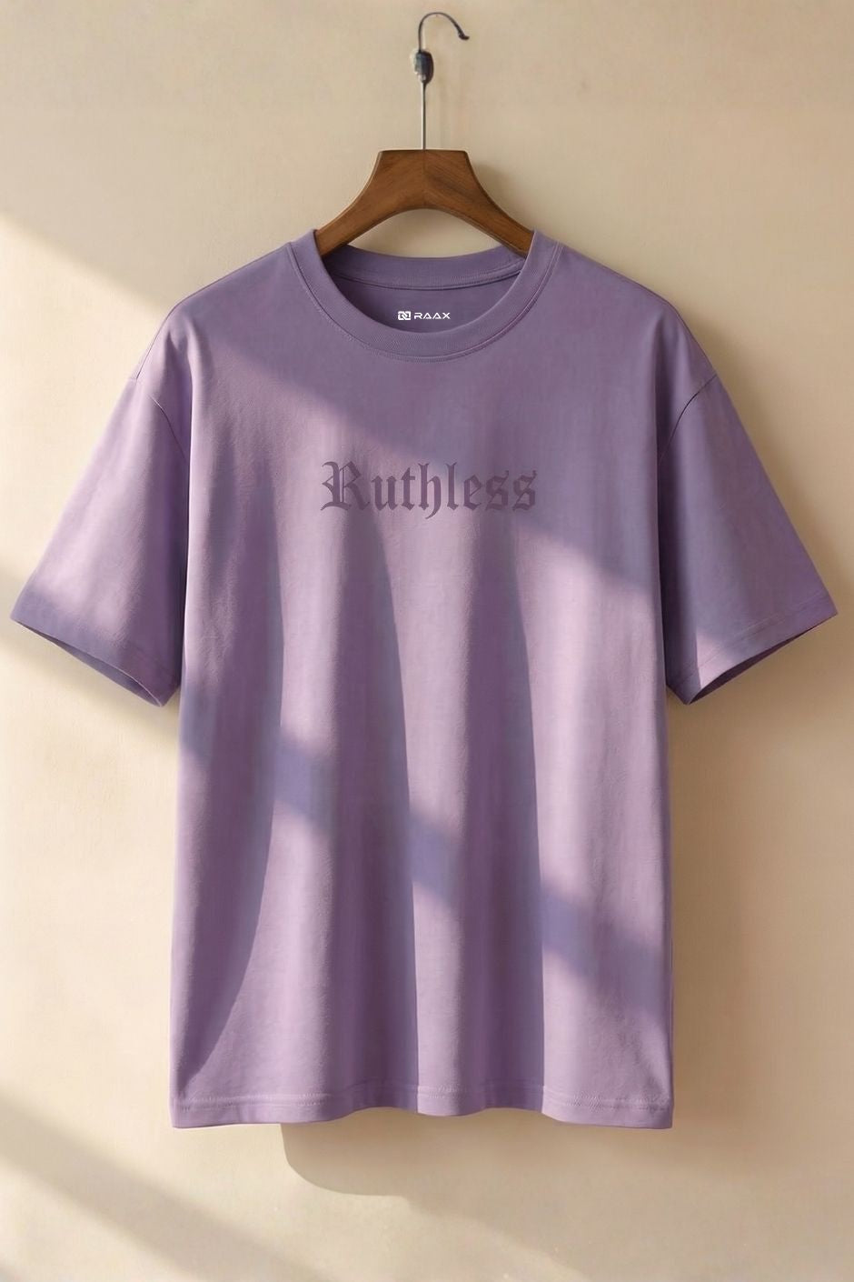 Lilac t-shirt with 'Ruthless' text on a hanger against a beige wall