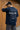 Person wearing a pastel blue t-shirt with 'Savage State' print, standing against a wooden wall.