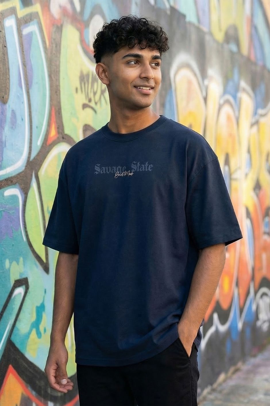Man wearing a pastel blue t-shirt with text in front of a colorful graffiti wall.