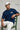 Man wearing a pastel blue t-shirt with a logo, sitting on a green chair against a gray background.