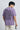 Person wearing a lilac t-shirt with text on the back, holding sunglasses, against a plain background