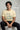 Man wearing a offwhite t-shirt with a graphic design and text, sitting on a white stool.