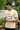 Man wearing a offwhite t-shirt with a graphic and text, standing outdoors.