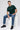 Man sitting on a white cube wearing a bottle green 'New York' t-shirt, blue jeans, and black shoes.