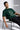 Man wearing a bottle green t-shirt with a graphic design, sitting on a chair against a plain background.