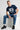 Man wearing a pastel blue t-shirt with 'SFCA' text and graphics, sitting on a white cube.