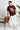 Man wearing a maroon red t-shirt with graphic design, standing next to a brown chair on a white background.