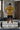 Person in a gym wearing a mustard yellow 'Trust' t-shirt, black shorts, and headphones, standing with a barbell.