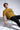 Man wearing a mustard yellow t-shirt with 'TRUST' printed on it, sitting on a chair against a white background.