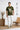 Man wearing a olive t-shirt with a graphic design, standing in a minimalistic room with wooden furniture.