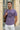 Man wearing a lilac t-shirt with text, standing outdoors against a beige building.