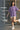 Person wearing a lilac t-shirt with text, standing outdoors near a metal gate.