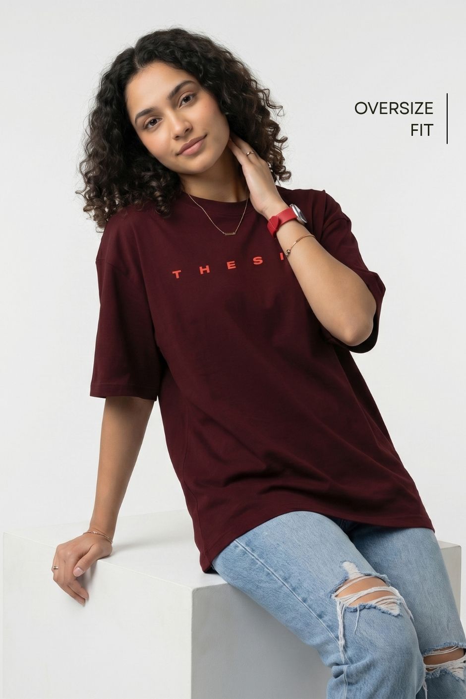 Woman wearing an oversized maroon red t-shirt with red text and light blue jeans on a white background.