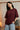 Person wearing a maroon red t-shirt with 'THESIS' text, standing in a room with curtains and a vintage television.