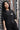 Person wearing a black t-shirt with 'TIME LESS' text against a textured wall.